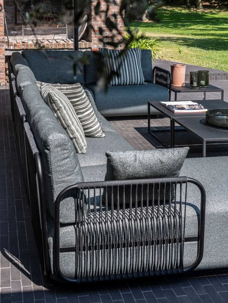 Modernes Outdoor-Lounge-Set aus dunkelgrauen Polstersofas mit anthrazitfarbenem Geflecht und Metallrahmen, im sonnigen Gartenambiente arrangiert.