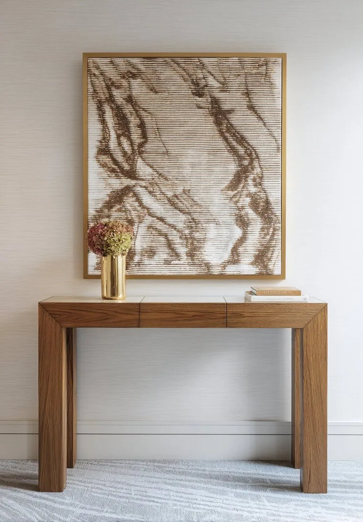 Schmale Konsole aus hellem Eichenholz mit goldener Vase und Büchern, darüber gerahmtes Wandbild in Braun- und Beigetönen.