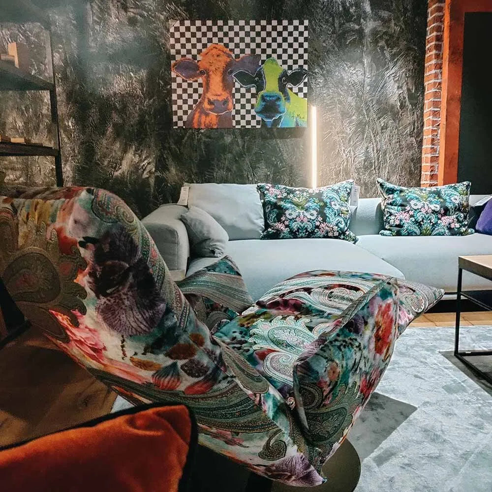 Modernes Wohnzimmer mit gemustertem Sessel und cognacfarbenem Sofa, gerahmtes buntes Wandbild auf strukturierter dunkler Wand