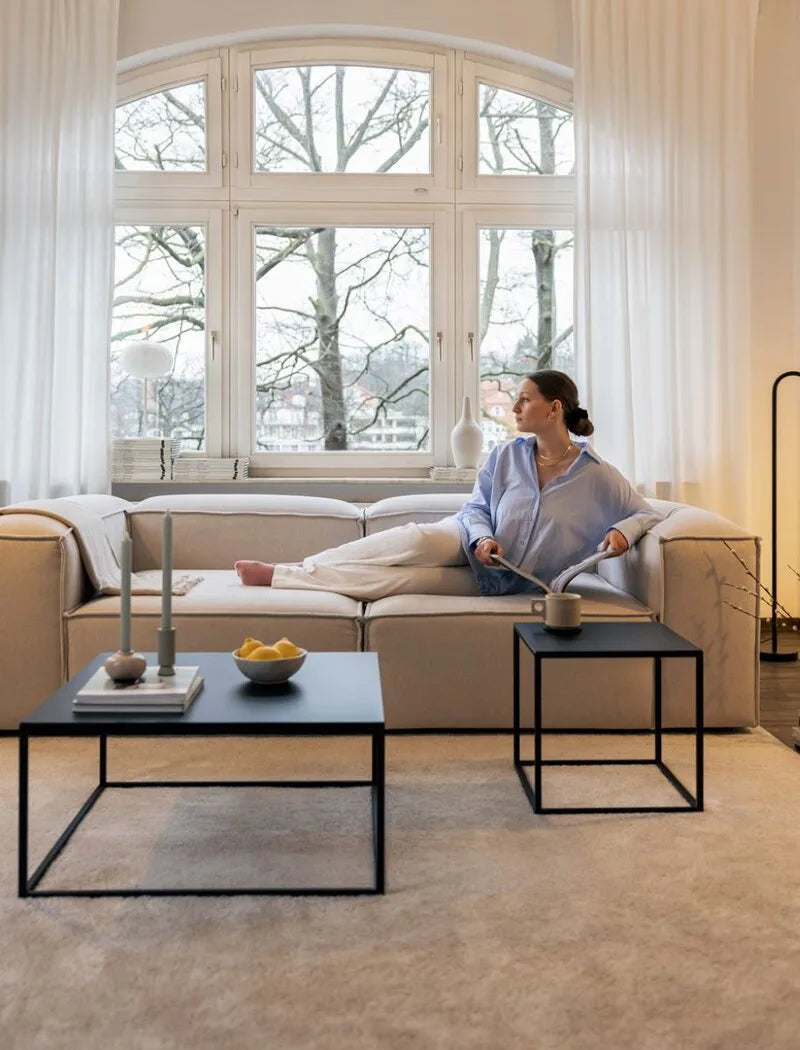 Metallbude Couchtische mit schwarzen filigranen Metallrahmen und dunklen Tischplatten vor einem beigefarbenen modularen Sofa im hellen Wohnzimmer.